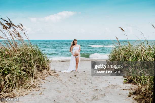 schöne schwangere frau mit entblößtem bauch in fließendem kleid in idyllischer strandlage, hoffnung vorfreude und neues leben - beautiful perfection exposed lady stock-fotos und bilder