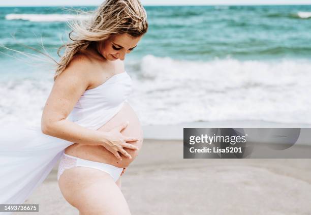 beautiful pregnant woman with exposed belly in flowing dress in an idyllic beach location, hope anticipation and new life - beautiful perfection exposed lady imagens e fotografias de stock
