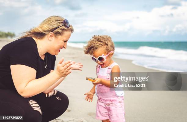 cute joyful mixed race toddler girl playing with her mom on an idyllic beach holiday - baby swimmer stock pictures, royalty-free photos & images