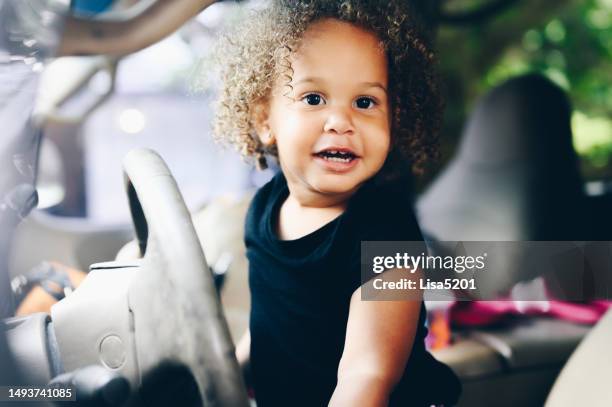cute happy mixed race toddler pretending to drive the family car - baby girls stock pictures, royalty-free photos & images