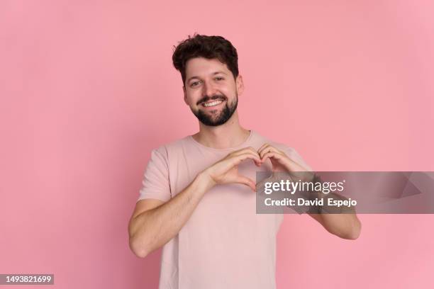 valentine's day concept. handsome young bearded man, gesturing heart sign and saying i love you, on pink background. - love you stockfoto's en -beelden