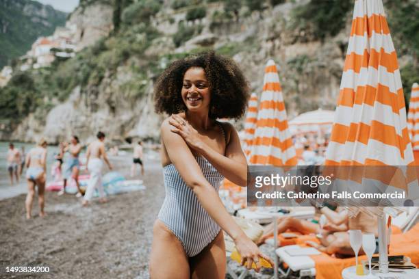 a beautiful young woman applies spray suncream on a sunny beach - protection luxe stock-fotos und bilder