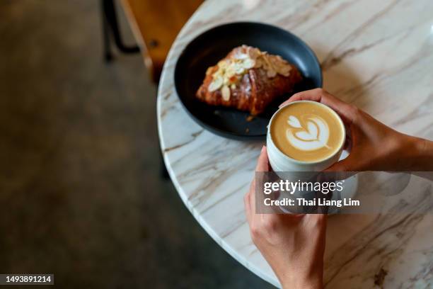 over the shoulder view of an asian woman enjoying her breakfast, a croissant with a cup of coffee in a cafe during the morning - coffees stock pictures, royalty-free photos & images