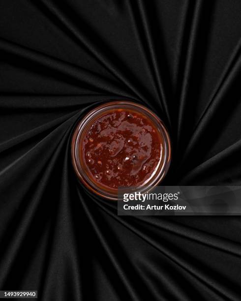 round jar of spicy red sauce on black sack. jar without lid in center, fabric is folded. view from above. black background. copy space - barbeque sauce stock pictures, royalty-free photos & images