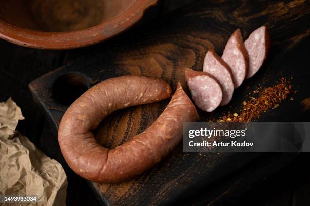 half-smoked sausage ring. sausage is cut into circles with spices on wooden board. homemade sausage. dark wooden background with wrapping paper and clay plate. view from above. soft focus - sausages stock pictures, royalty-free photos & images