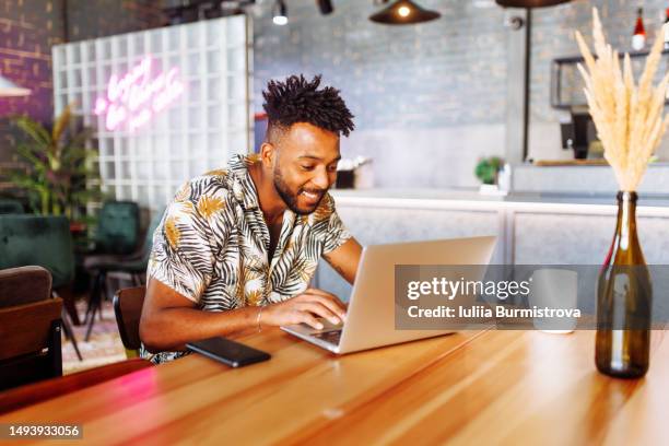 young businessman of west asian origin starting workday in local cafe sitting at table and typing on laptop - dark skin tone stock pictures, royalty-free photos & images