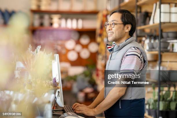 streamline to reduce overhead costs to improve your small business profit margins. side view of a japanese show owner at a cashier counter waiting for customers entering to buy products in the furniture and home decor store. - personalizzazione foto e immagini stock