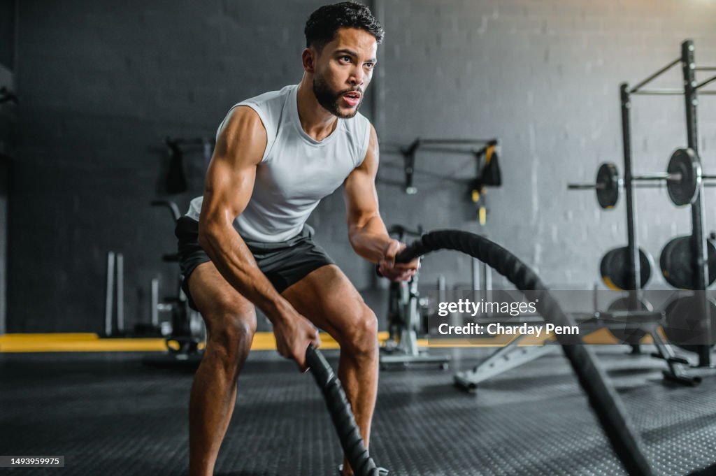 Young man working out with battle ropes in gym