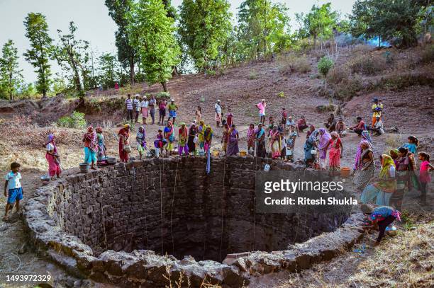 Women draw water from a partially dried up well using plastic containers attached to ropes on May 26, 2023 in Khokher Viheer village, Peth Taluka,...