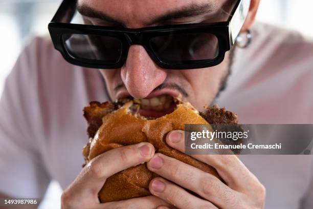Man bites a bacon cheeseburger at Meat Crew fast food restaurant on May 28, 2023 in Milan, Italy. On occasion of the World Burger Day, celebrated on...