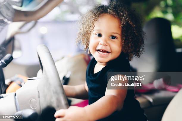 cute happy mixed race toddler pretending to drive the family car - funny baby photo stock pictures, royalty-free photos & images