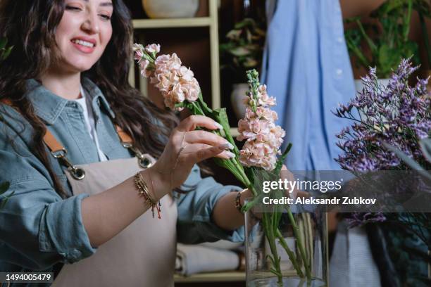 a young woman, a professional florist takes care of flowers in a cozy flower shop and collects beautiful modern bouquets. floristry, small business. the concept of retail, private business, startup. a seller in a flower shop creates a creative bouquet. - turkish ethnicity bildbanksfoton och bilder