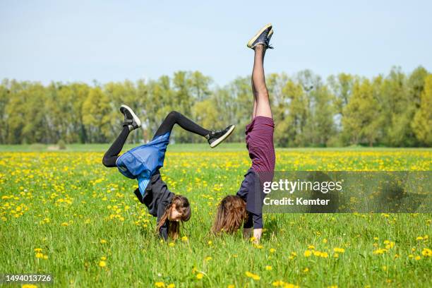 two teenage girls making handstand outdoors - girl in dress doing handstand stockfoto's en -beelden