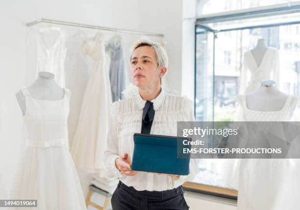 store manager standing in her bride boutique and taking inventory on digital tablet - designer clothing stock pictures, royalty-free photos & images