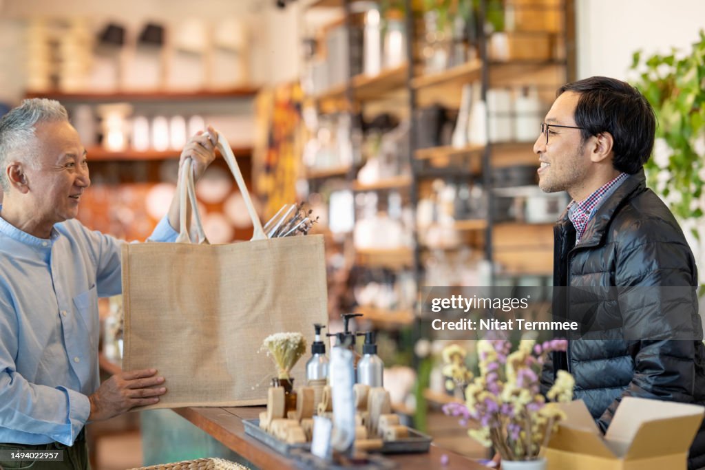 Improved Customer Loyalty to Effective Retention Strategies for Your Small Business. A Japanese show owner handing a reusable bag to a smiling customer after checkout at a cashier counter in a home decor store.