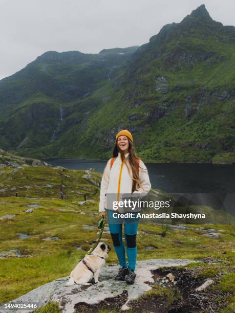 happy woman with dog contemplating a hiking outdoors on lofoten islands - extreem weer stock pictures, royalty-free photos & images