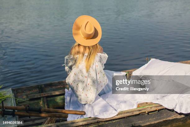 blonde woman in white dress enjoying vacation on the lake. white linens in old fishing boat with oar. bed sheets. summer relaxation - human back stock pictures, royalty-free photos & images