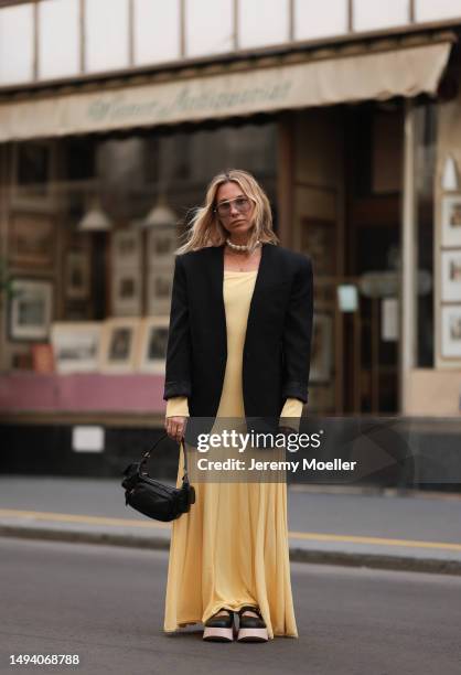 Karin Teigl wearing Jacquemus long cotton yellow pastell dress, Mugler x H&M black oversized blazer, MiuMiu Pocket black leather bag and AGL plateau...