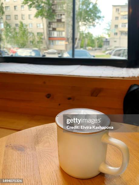 a cup of cappuccino with a pattern in a cafe on a wooden table against the background of a wide window - crema stock pictures, royalty-free photos & images