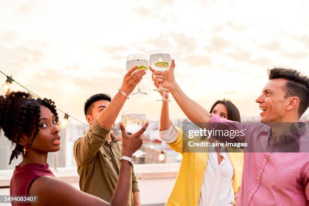 group photo of four friends in casual clothes, celebrating and making toasts with joy, on the rooftop at sunset. - asian female friends drinking soda outdoor stock pictures, royalty-free photos & images