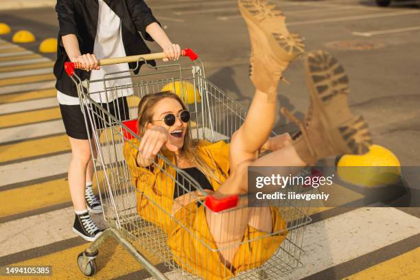 dos jóvenes rubias se divierten con el carrito de compras. mujer de moda - consumismo fotografías e imágenes de stock