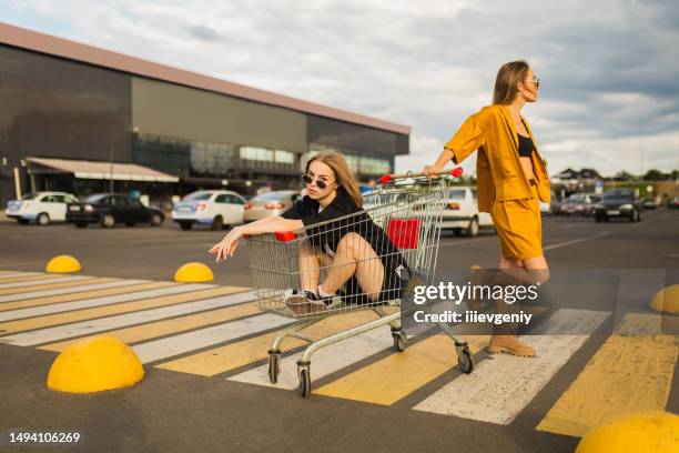 dos jóvenes rubias se divierten con el carrito de compras. mujer de moda - fashion model bag fotografías e imágenes de stock