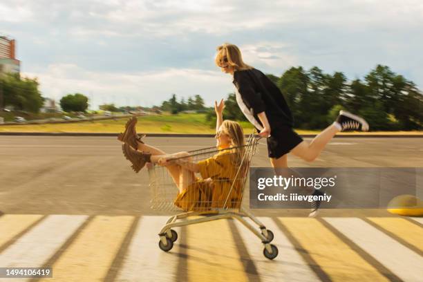 deux jeunes filles blondes s’amusent avec le caddie. mode femme - chariots et charrettes photos et images de collection