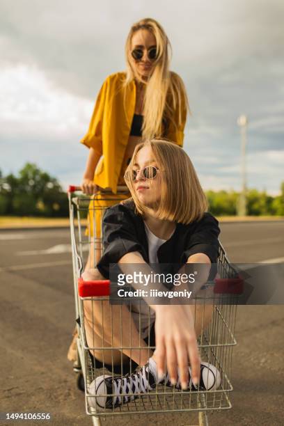two young blonde girls have fun with shopping cart. fashion woman - generation z shopping stock pictures, royalty-free photos & images
