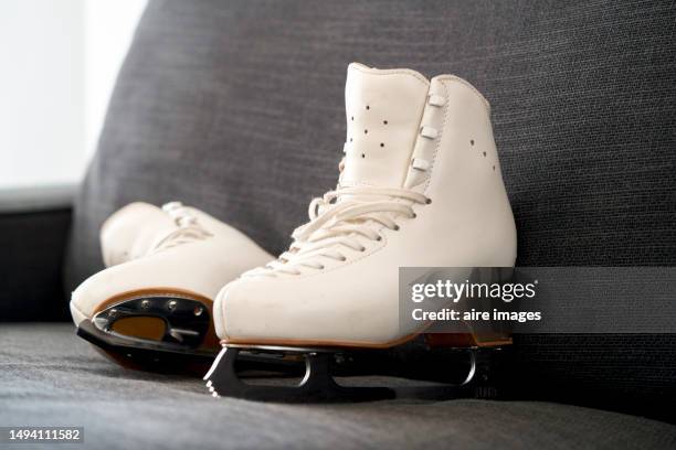 side view of a pair of white figure skating boots on the ground with metal blades, no people around. - leather training shoes stock-fotos und bilder