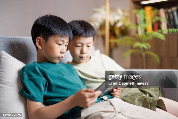 two asian boys sitting on the sofa using digital tablets - china games day 2 stock pictures, royalty-free photos & images