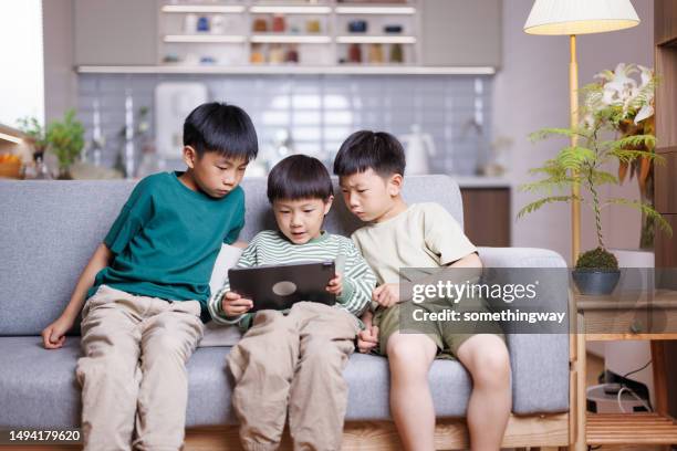 three asian boys playing games on digital tablets at home - china games day 4 stockfoto's en -beelden