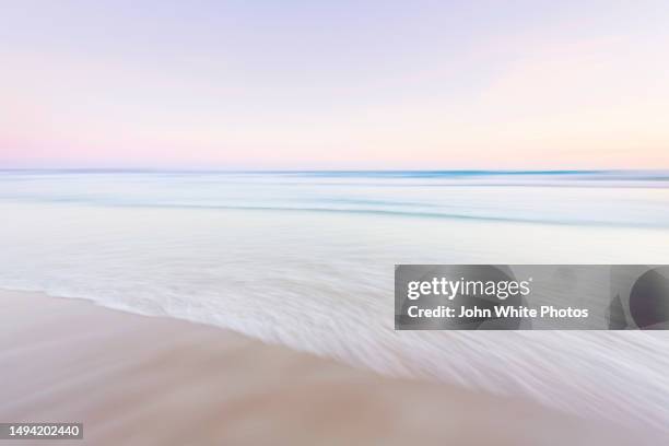 storm clouds and waves breaking onto a beach. intensional camera movement to blur clouds, beach, waves and the ocean to give a dream like abstract image. - seascape sunset stock pictures, royalty-free photos & images