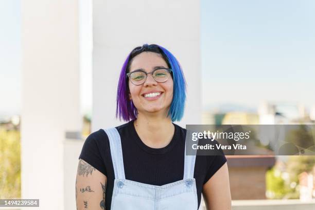 portrait of colombian lesbian woman with blue dyed hair smiling looking at camera - jeans latzhose frau stock-fotos und bilder