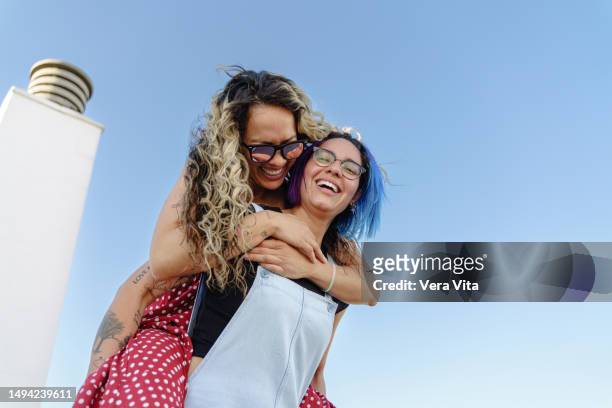 couple of gay young women with happiness carry on shoulders piggyback isolated on blue sky. - blue sky friends photos et images de collection