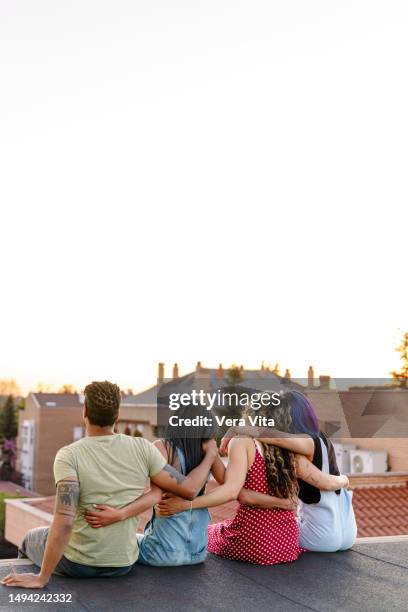 unrecognizable young friends hugging each other sit at terrace watching sunset in madrid city scape. - club nomadic ストックフォトと画像
