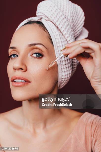 slow age skin routine: portrait of a beautiful smiling woman applying vitamin c serum on her face - maroon hair stock pictures, royalty-free photos & images