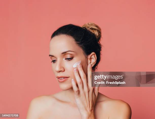 slow age skin routine: portrait of a beautiful happy woman with face cream on her cheek - face cream stock pictures, royalty-free photos & images
