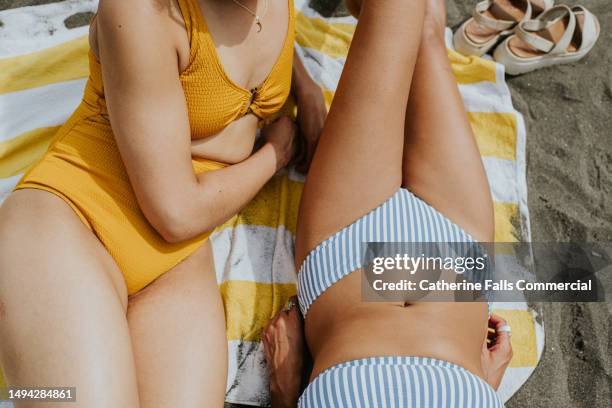 close-up top down image of two females sunbathing on a beach - swimming costume stock pictures, royalty-free photos & images