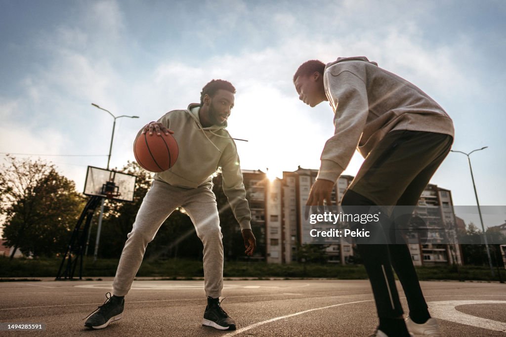 Friends playing one on one basketball on outdoor court