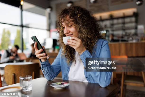 happy young woman using mobile phone and enjoying coffee at cafe - mobile cafes stock pictures, royalty-free photos & images
