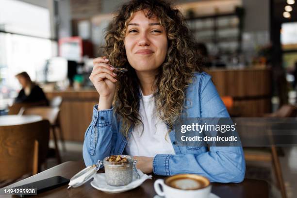 lächelnde junge frau, die chia-pudding zum frühstück im café isst - women yogurt stock-fotos und bilder