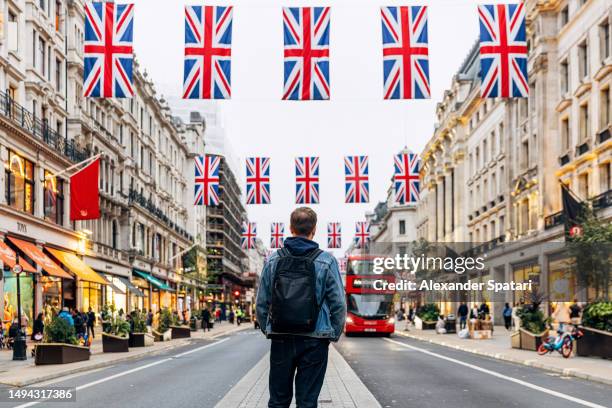 rear view of man with backpack standing on regent street decorated with british flags, london, uk - oxford street stock-fotos und bilder