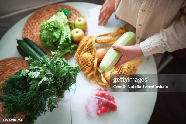 fresh and eco-conscious: captured from a top-down perspective, an unidentified woman extracts fresh organic vegetables, zucchini, and cucumbers from a tote bag on a well-lit kitchen table, embodying the principles of zero waste and environmental care. - plump girls stock pictures, royalty-free photos & images