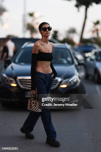 Soulin Omar seen wearing a black cropped top, black pants and black shades and a brown and white printed Prada handbag during the 76th Cannes film...