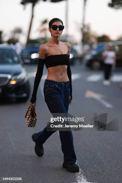 Soulin Omar seen wearing a black cropped top, black pants and black shades and a brown and white printed Prada handbag during the 76th Cannes film...