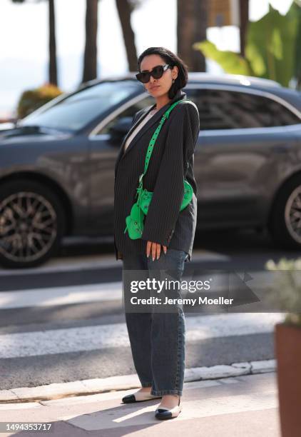 Amal Aouadi is seen wearing a white and black stripped oversized blazer, jeans pants, black Poppy Lissiman shades, silver earrings, green Balenciaga...