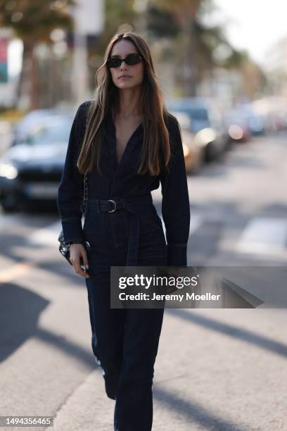 Film Festival Guest is seen wearing a blue denim overall, black shades and a belt and a black Chanel leather handbag during the 76th Cannes film...