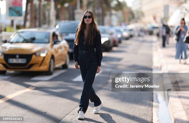 Film Festival Guest is seen wearing a blue denim overall, black shades and a belt and a black Chanel leather handbag during the 76th Cannes film...