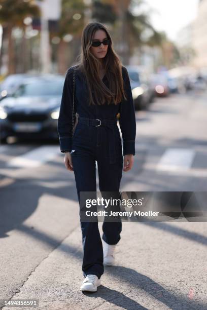 Film Festival Guest is seen wearing a blue denim overall, black shades and a belt and a black Chanel leather handbag during the 76th Cannes film...