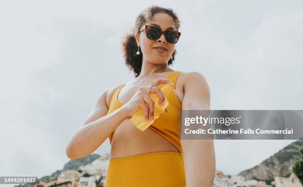 a woman spritzes sun screen onto her arm on a sunny day - parasol persoonlijk accessoire stockfoto's en -beelden